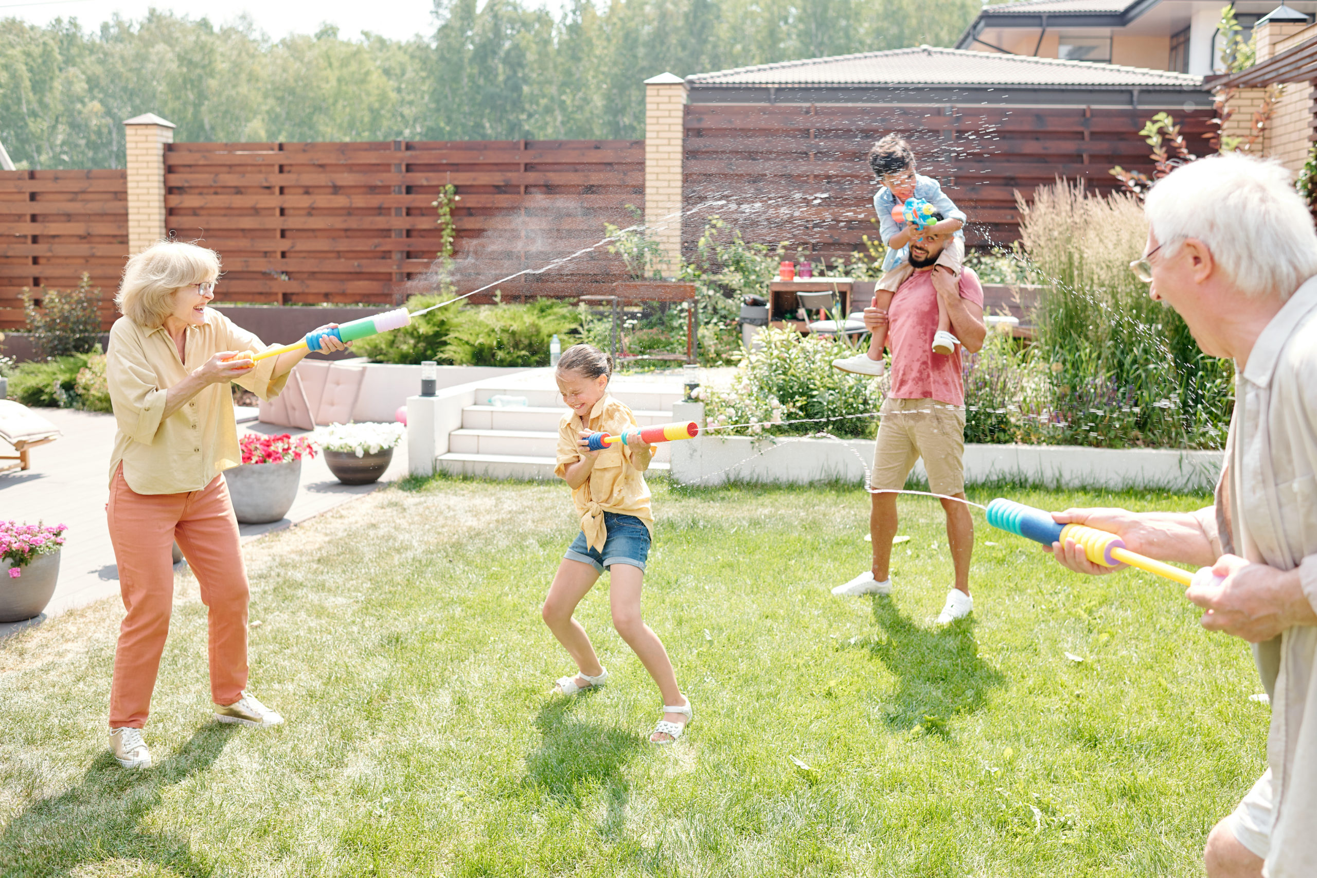 Familie beschießt sich mit Wasserspritzpistolen im Garten.