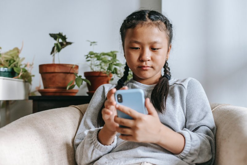 Ein junges Mädchen sitzt auf dem Sofa und hält ein Kinderhandy in der Hand. 